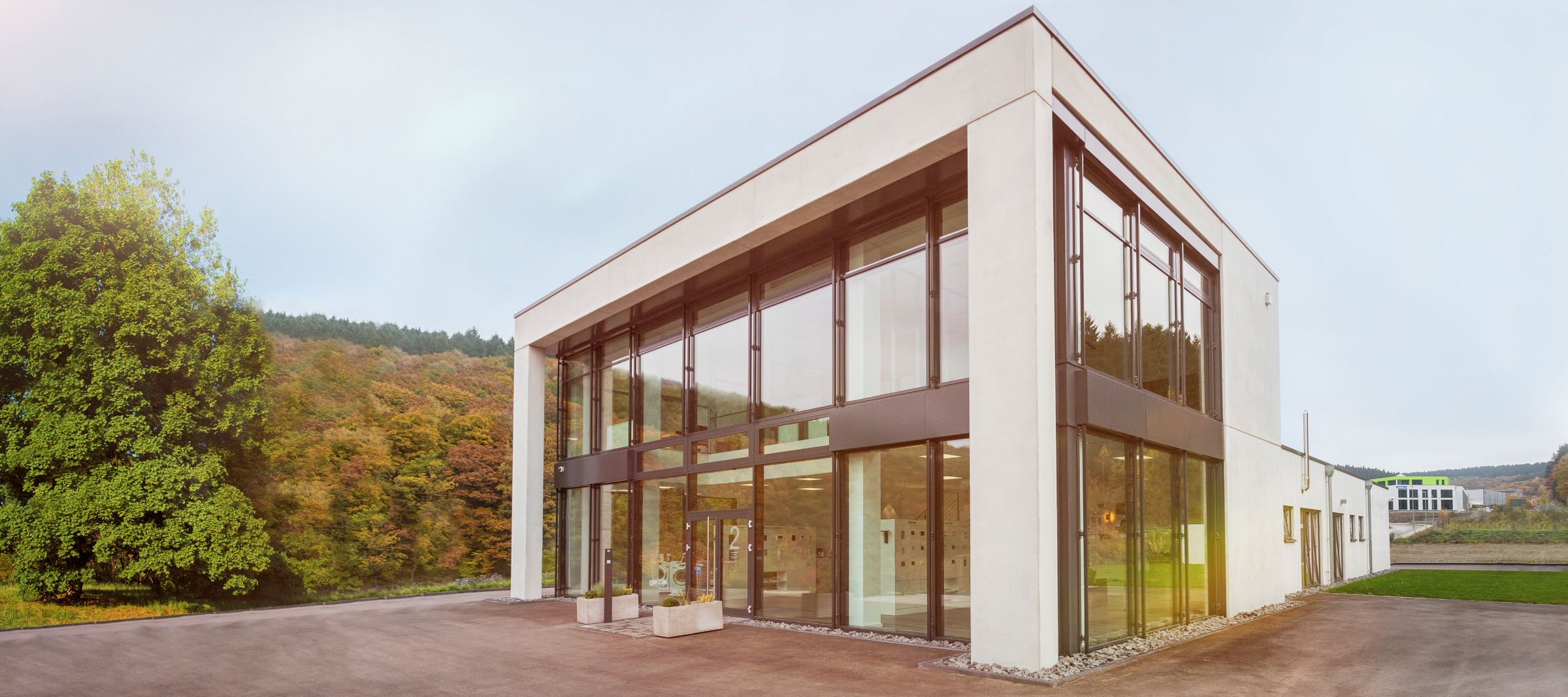 Firmengebäude der Gerhards Elektrotechnik GmbH in Siegen: heller, zweigeschossiger Bau mit großen Glasfassaden, daneben Bäume im Herbstlaub.