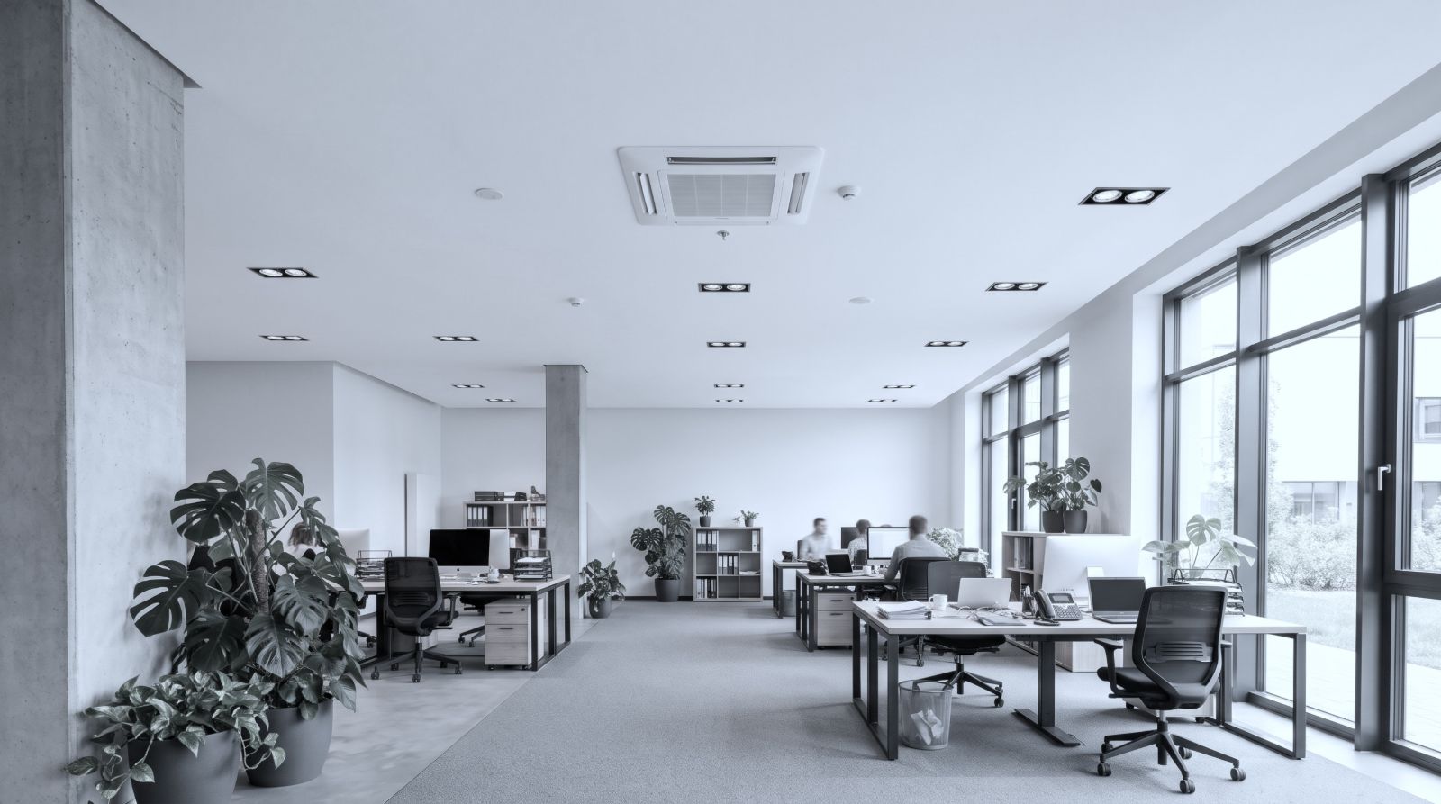 Heller Büroraum mit großen Fenstern und Arbeitsplätzen, in der Decke ein eingebautes Kassetten-Klimagerät.