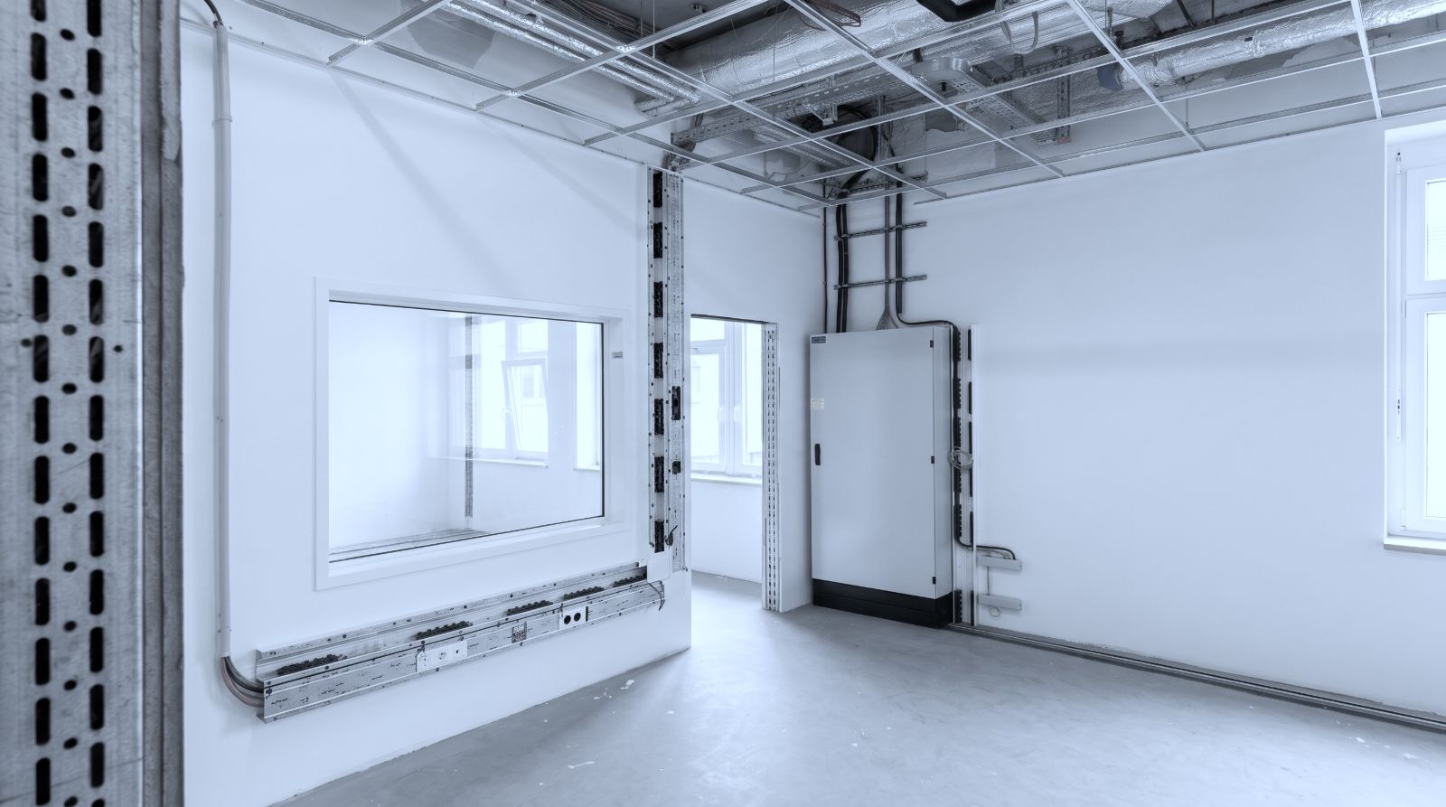 Medizinisch genutzter Raum in der Installationsphase: offene Deckenkonstruktion mit Kabeltrassen, eine Unterverteilung an der Wand und ein Brüstungskanal unter dem Sichtfenster.