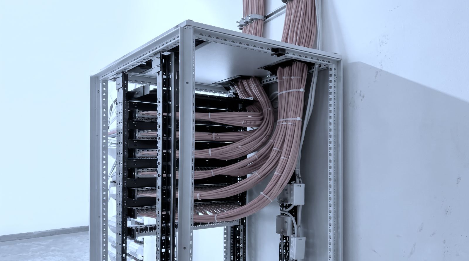 Netzwerkschrank in der Installationsphase: zahlreiche Datenleitungen sind gebündelt von oben eingeführt und zu den Patchfeldern geführt.