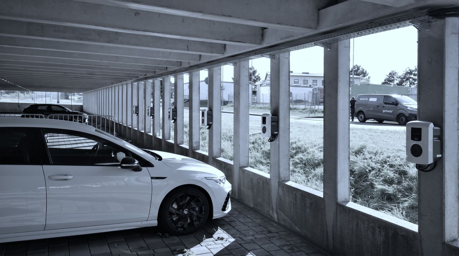 Überdachtes Parkdeck mit mehreren Wallboxen an den Stützen, im Vordergrund ein geparktes Auto.